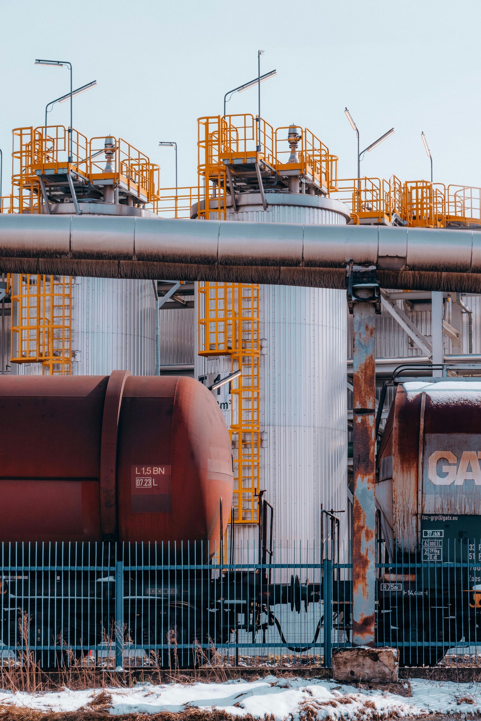 A train is parked in front of a building with a lot of pipes.