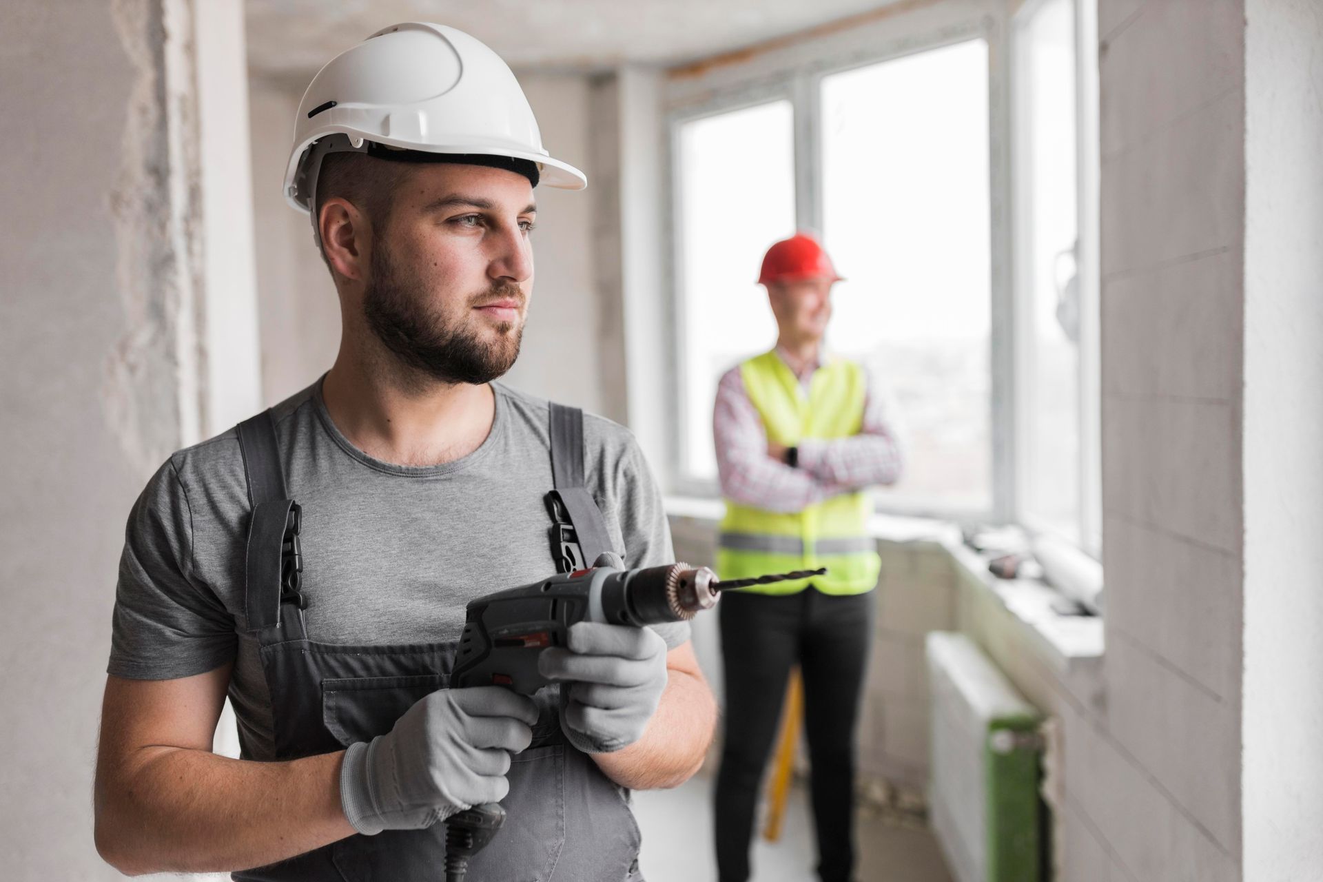 a man is holding a drill in his hand while another man stands in the background .