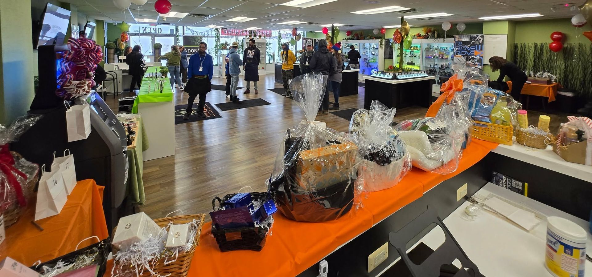 Retail store checkout area with an orange display table of wrapped gift baskets and shoppers in the background