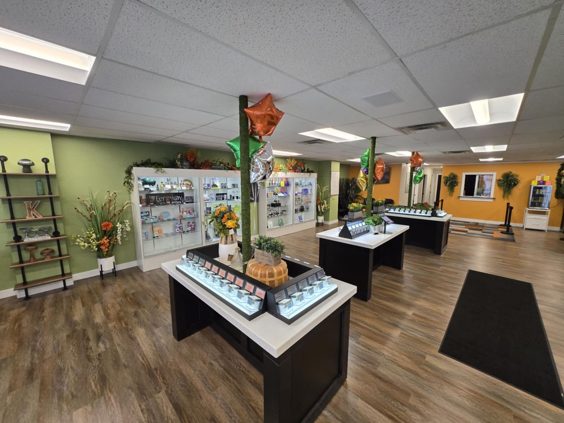 Bright gift shop with display tables, shelves, and a black entrance mat on wood flooring.