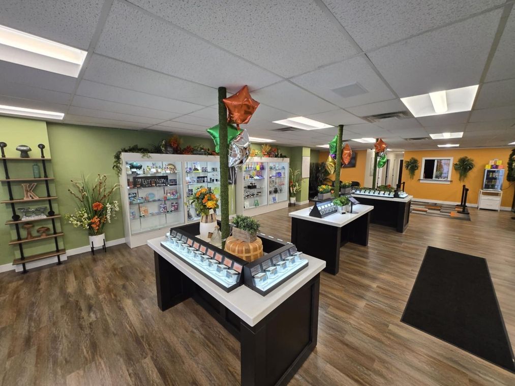 Bright gift shop with display tables, shelves, and a black entrance mat on wood flooring.