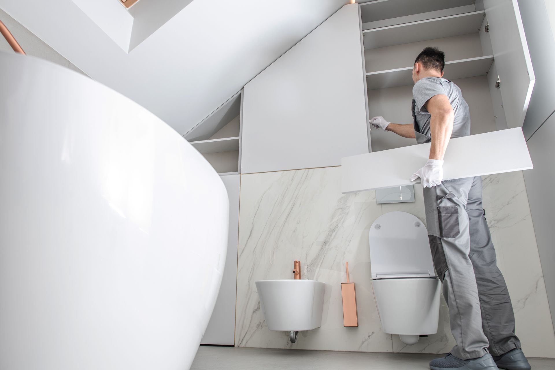 A man holding a cabinet piece stands in a bathroom, positioned between a toilet and a sink.