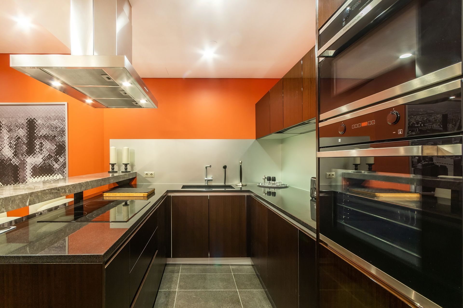 A modern kitchen featuring orange walls and stainless steel appliances.