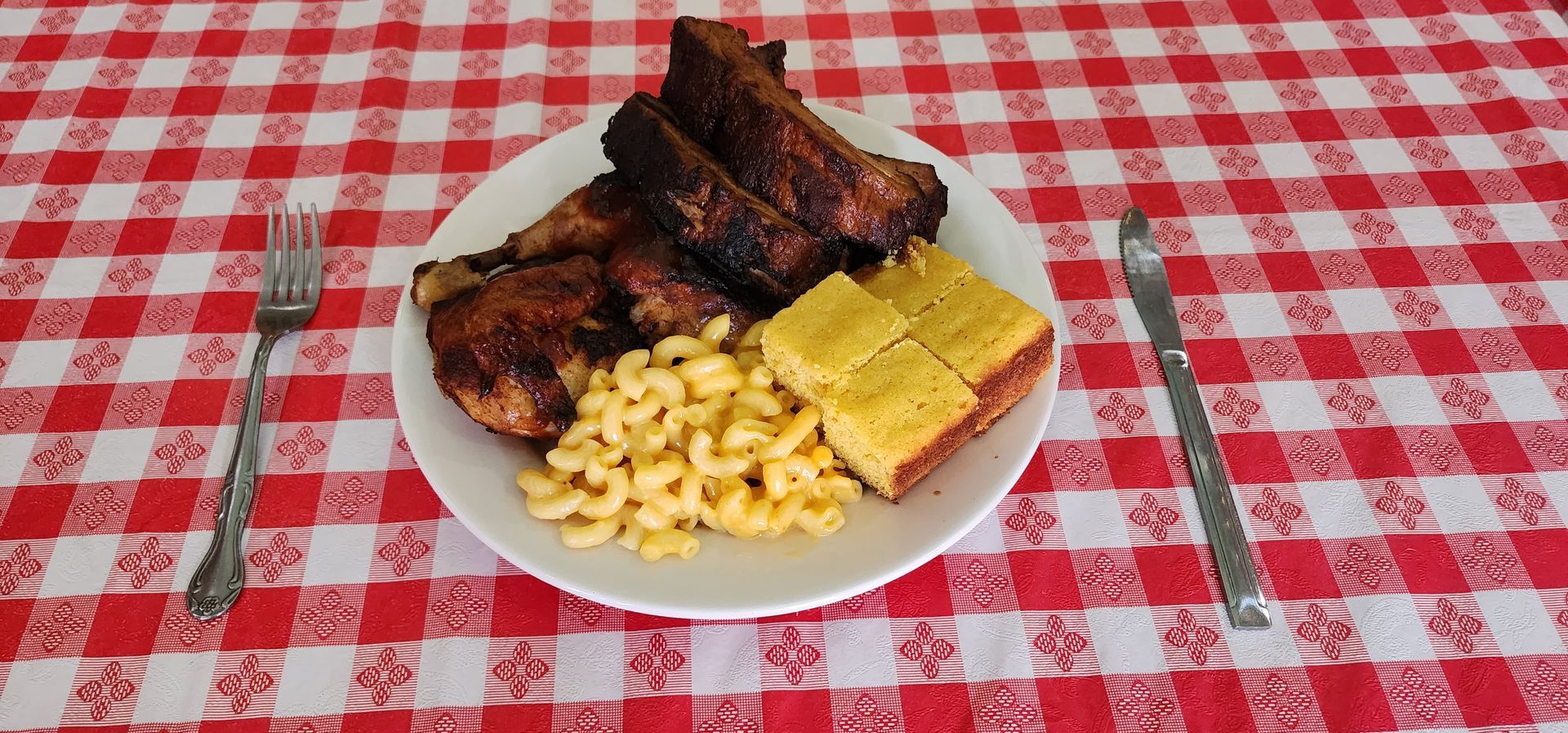 Plate of grilled ribs, corn on the cob, and pasta on a red checkered tablecloth