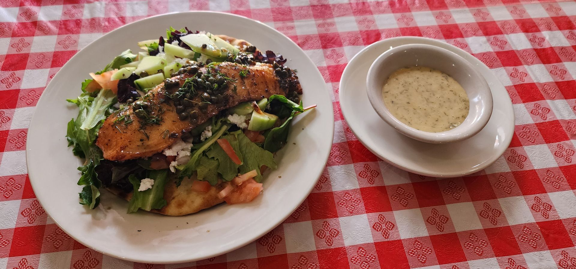 Salad plate with grilled salmon and a side of dressing on a red checkered tablecloth
