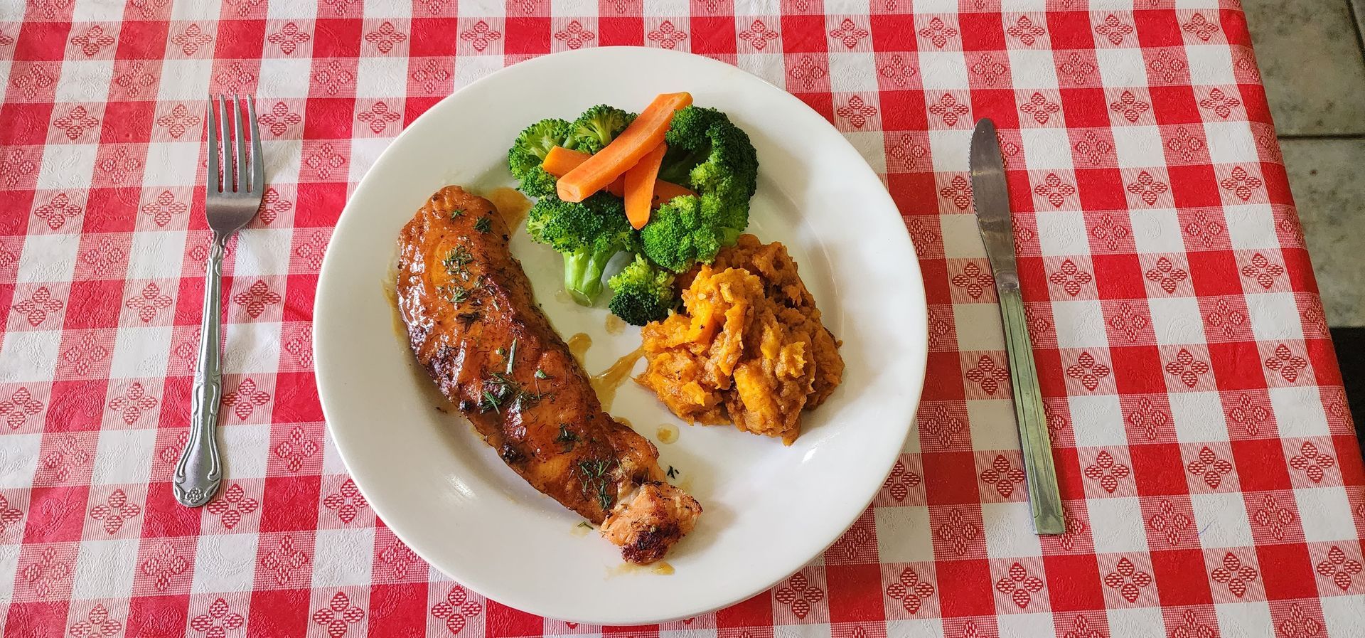 Plate of grilled meat, rice, and vegetables on a red-and-white checkered tablecloth