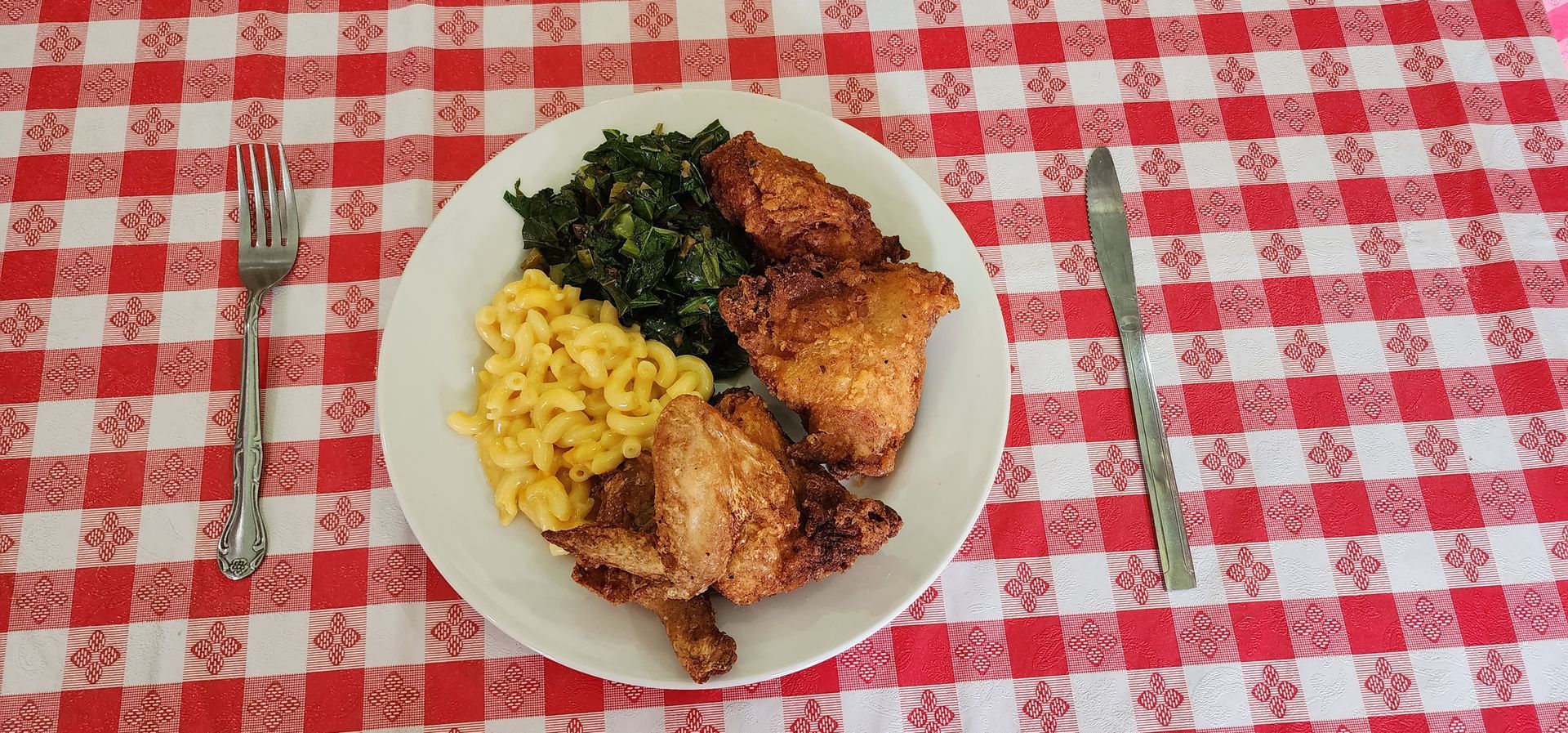Plated roasted chicken with rice and greens on a red-and-white checkered tablecloth, with a fork and knife beside it