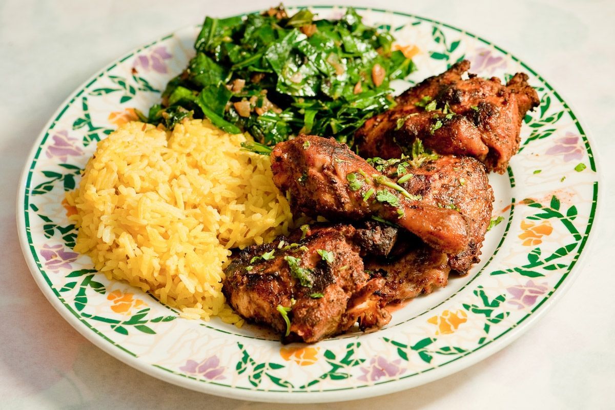 Plate of yellow rice, roasted chicken, and sautéed greens on a floral dish