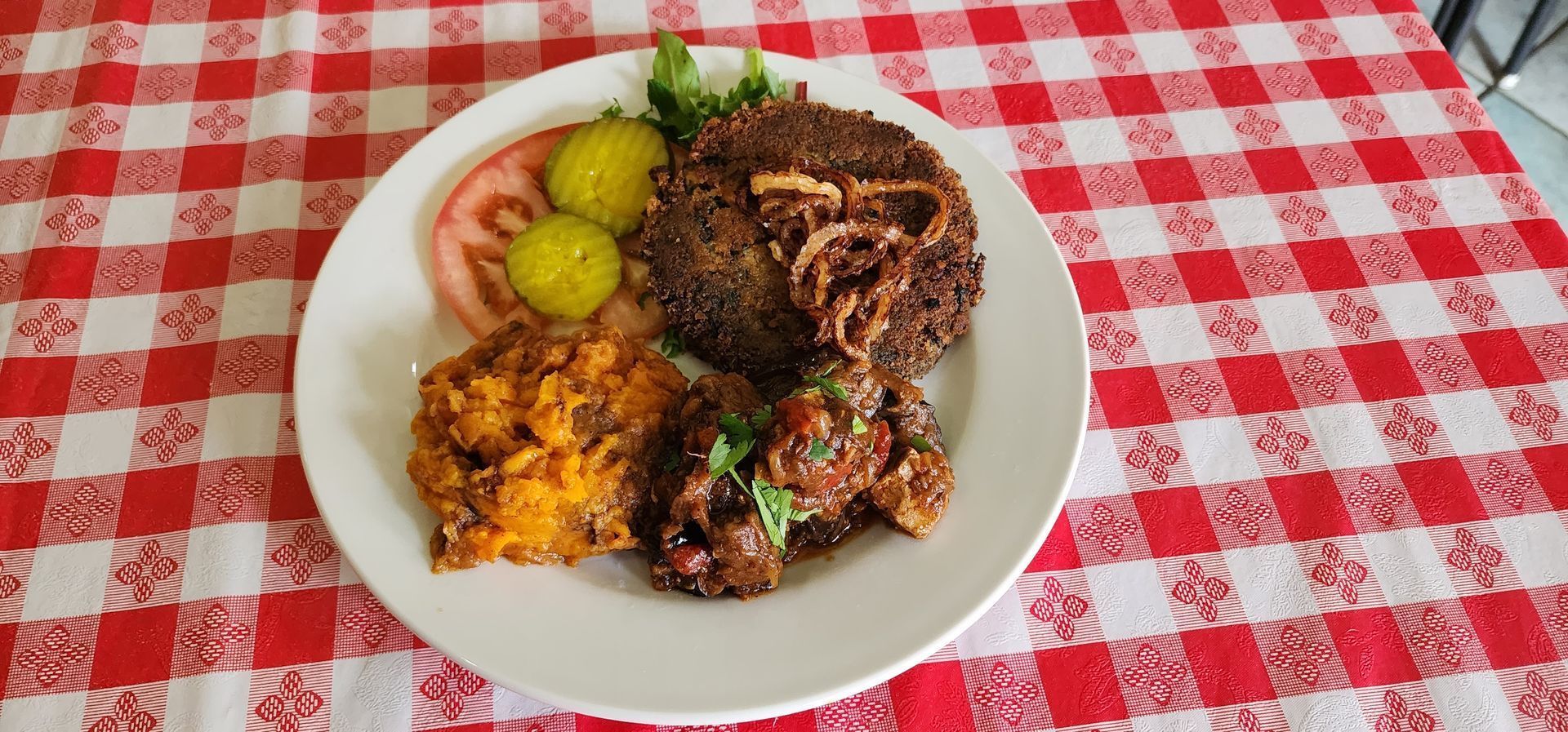 Plate of rice, stewed meat, fried plantains, and side vegetables on a red-checkered tablecloth