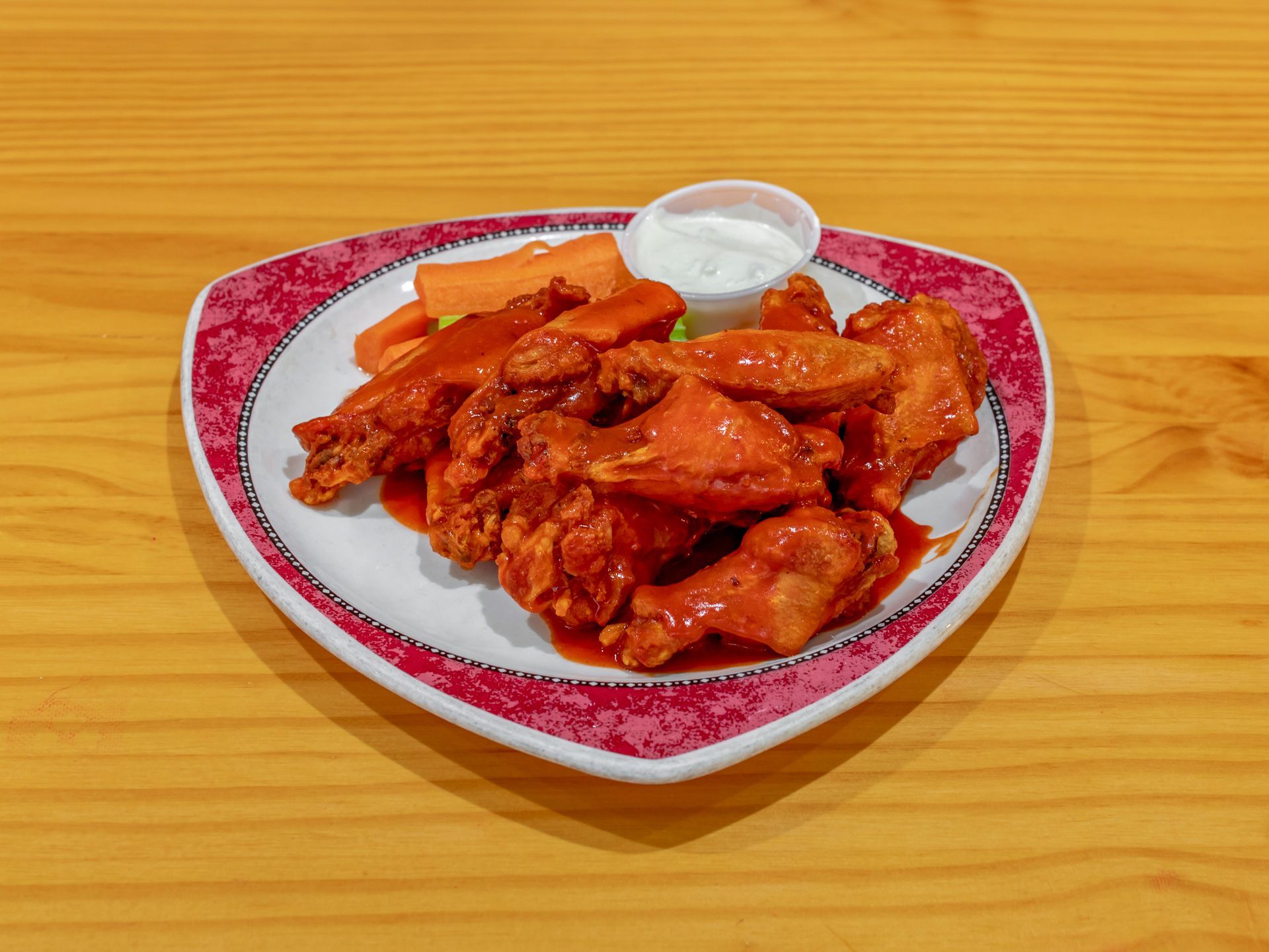 Plate of saucy chicken wings with dipping sauce on a red heart-shaped plate