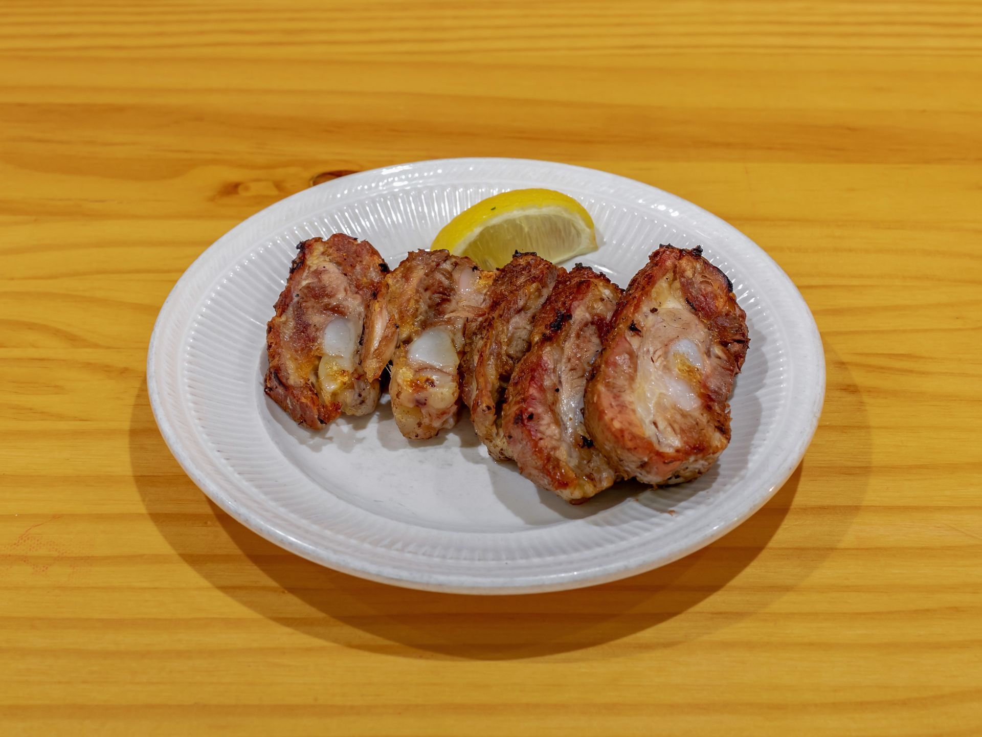 Plate of grilled chicken slices with a lemon wedge on a wooden table