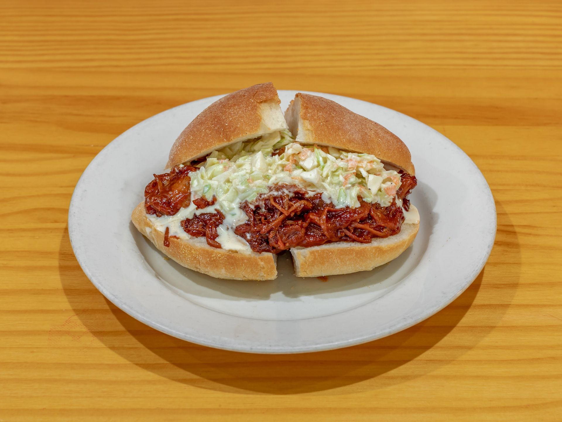 Sandwich with shredded meat and cabbage on a white plate on a wooden table