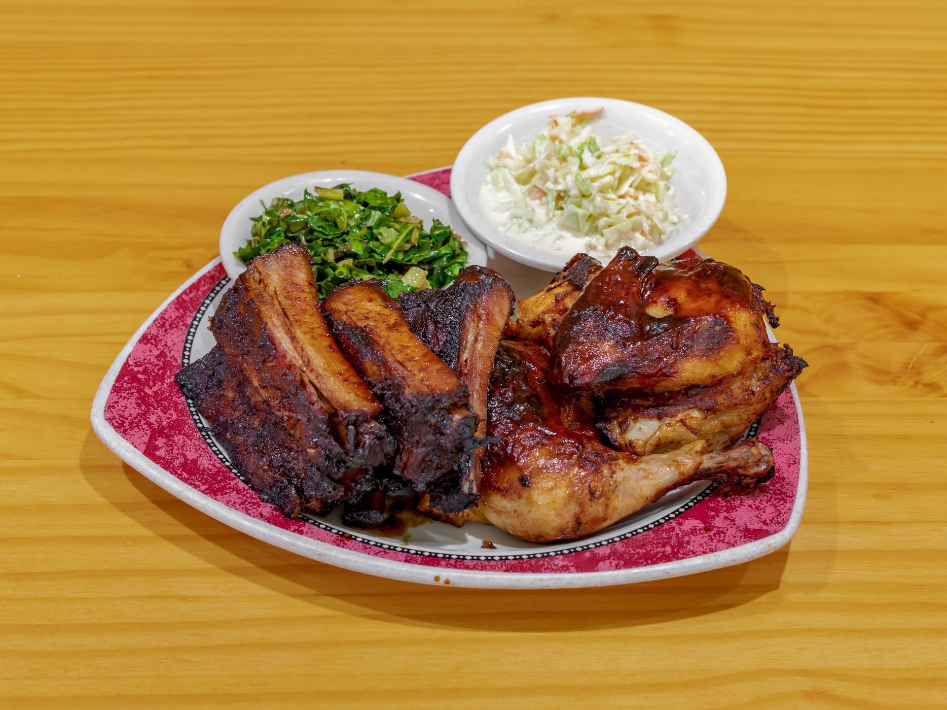 Plated grilled meat with greens and coleslaw on a pink patterned dish over a wooden table