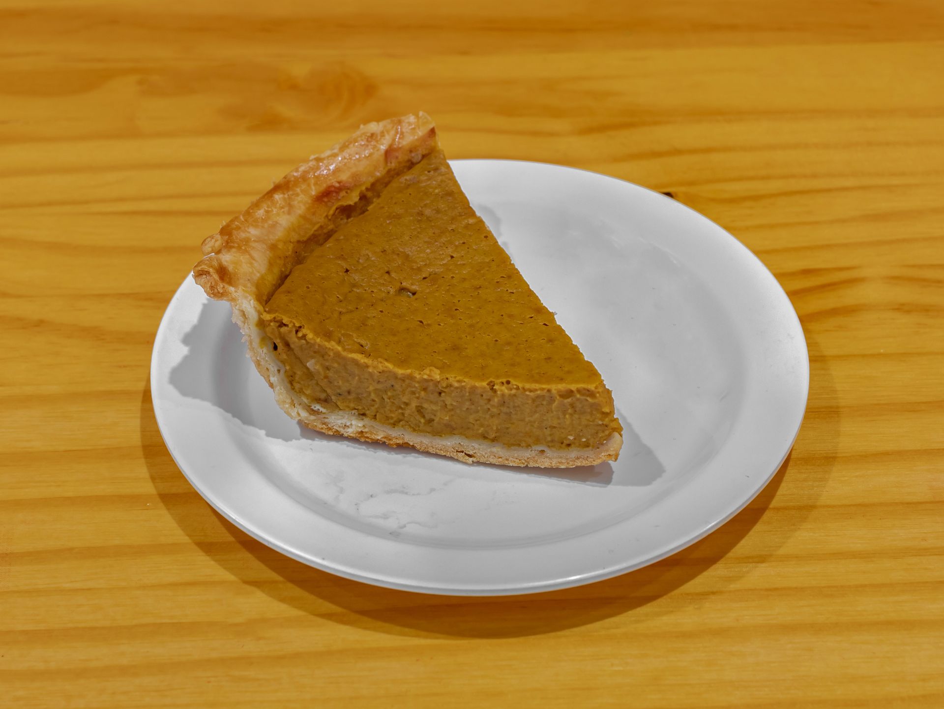 Slice of pumpkin pie on a white plate atop a wooden table