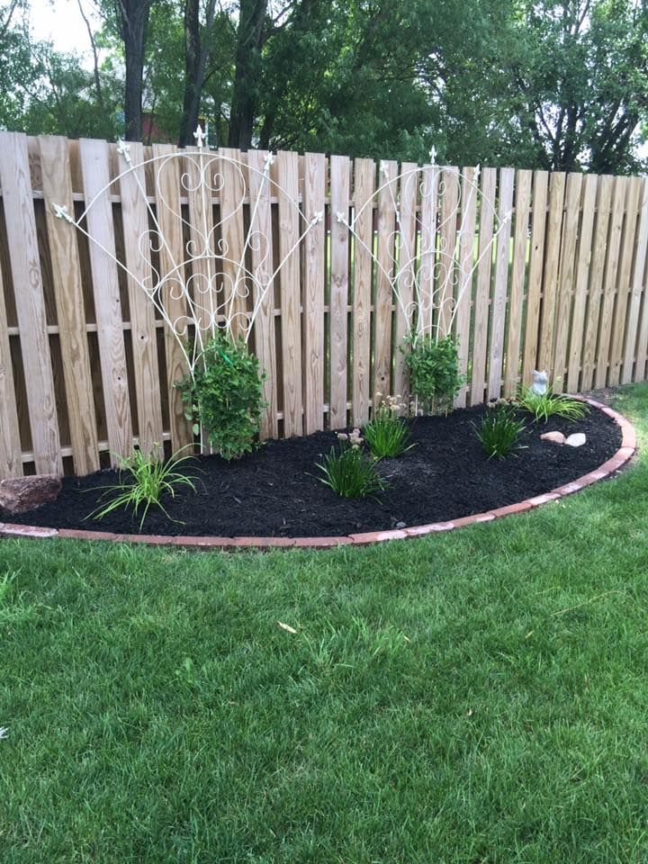 Stone retaining wall with white flowers and shrubs beside a green lawn and house steps
