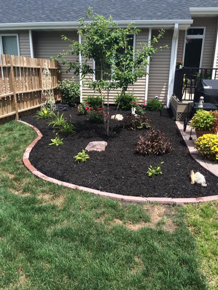 Modern backyard walkway with concrete pavers, gravel border, and a row of green shrubs along a wall