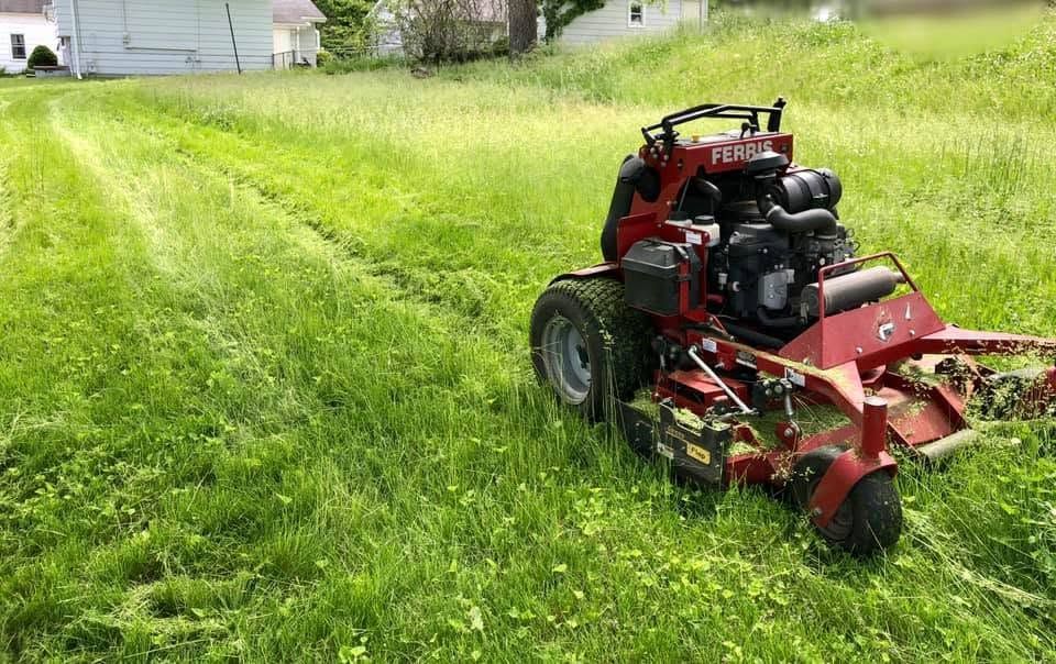 Red riding lawn mower spraying grass along a curb in a sunny yard