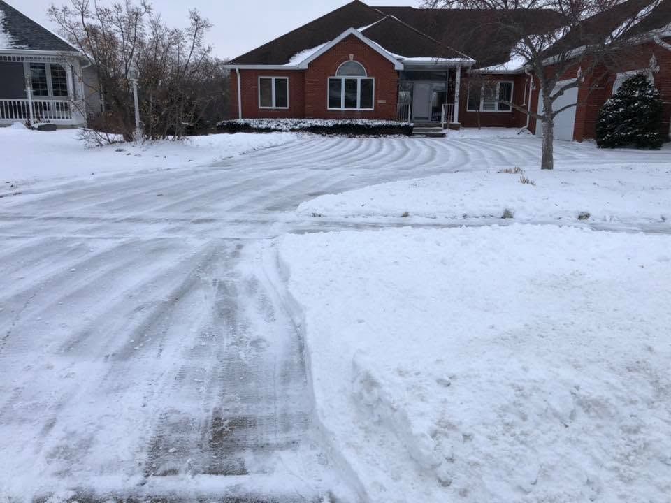 Person shoveling a snowy driveway beside a suburban house at sunset