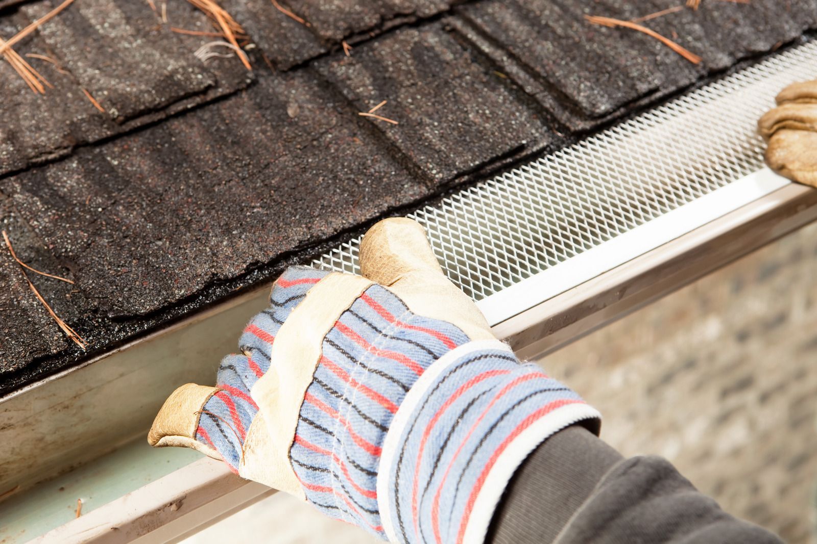 Gloved hand installing a white gutter guard on a roof edge