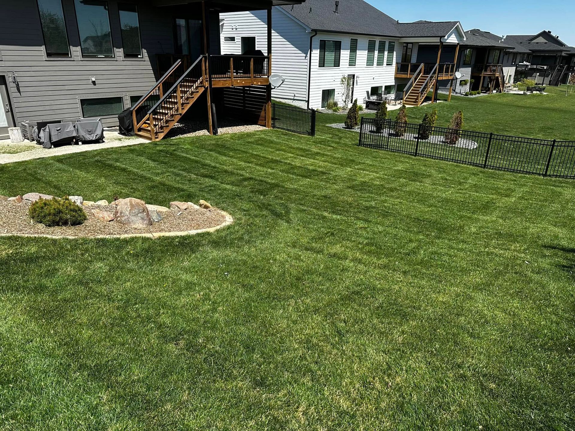 Backyard with green lawn, stone bed, and raised decks behind a fence of suburban homes