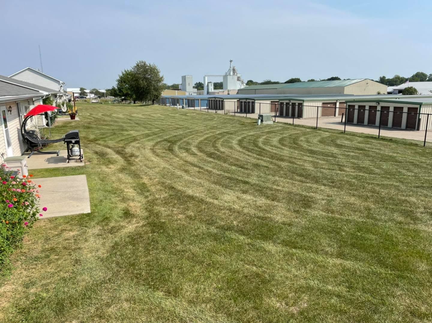 Wide grassy field beside school buildings, with a person mowing near the left edge on a sunny day.