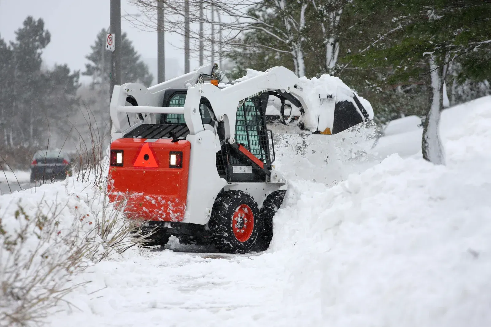 Snowy nighttime scene with a red construction loader and gray dump trailer outside apartment buildings