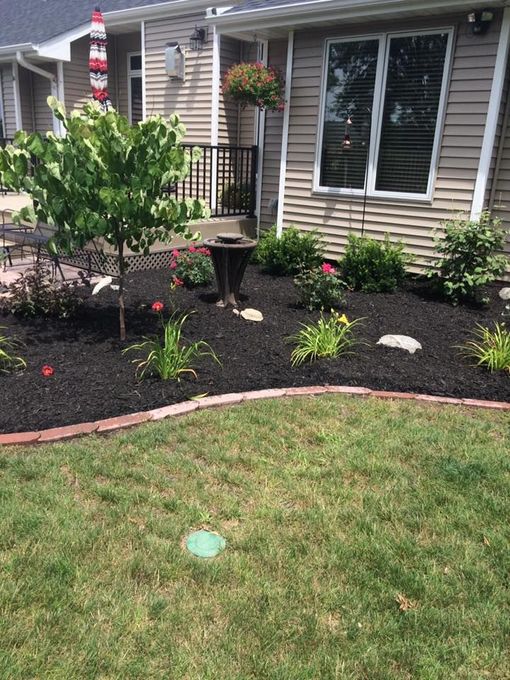 Front yard garden with mulch beds, pink flowers, hanging basket, and a house with windows and brick trim