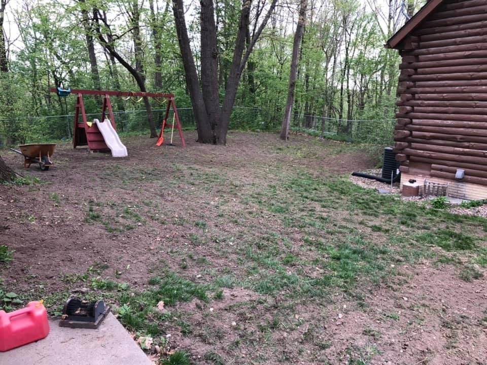 Wooded backyard with a red swing set, slide, and log cabin deck