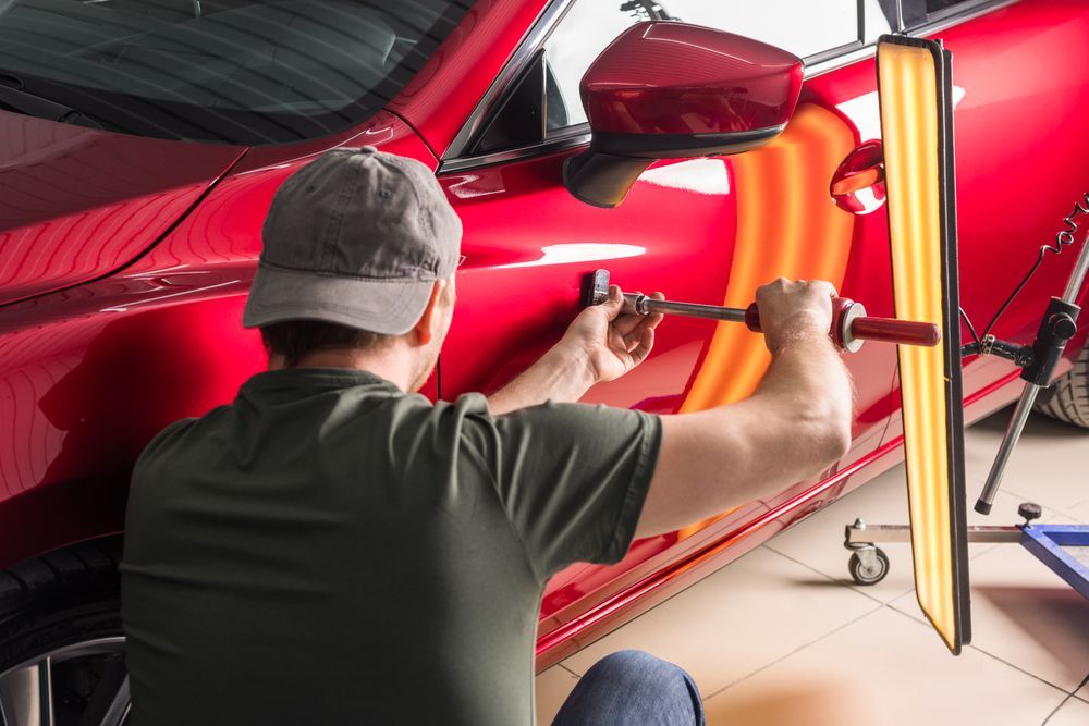 Person Using Tools to Remove a Dent From a Red Car Door in a Garage — Bowen Automotive in Bowen, QLD