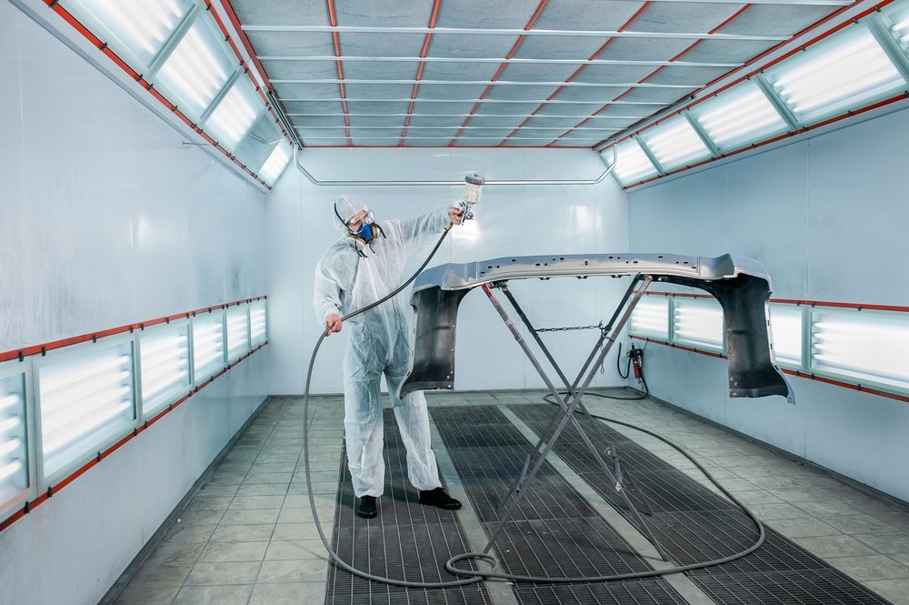 Person in Protective Suit Spraying Paint on Car Part — Bowen Automotive in Bowen, QLD