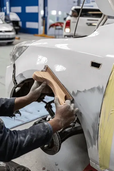 Hands Sanding Bodywork on a White Car Fender in a Repair Shop — Bowen Automotive in Bowen, QLD