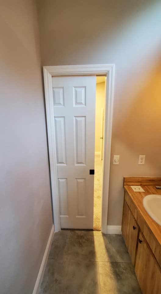 A white, six-panel pocket door is partially open, revealing a view into a brightly lit interior space.