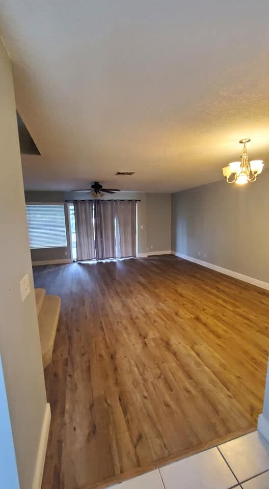 An open-concept living area with light wood-style flooring, gray walls, a ceiling fan, and sliding glass doors.