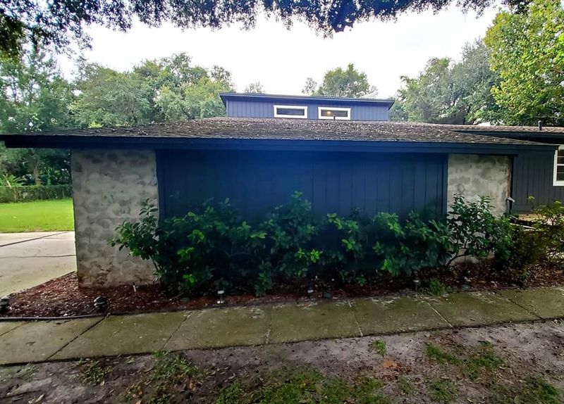 A mid-century modern home exterior with blue paneling, natural stone walls, a low-slung roof, and small clerestory windows.