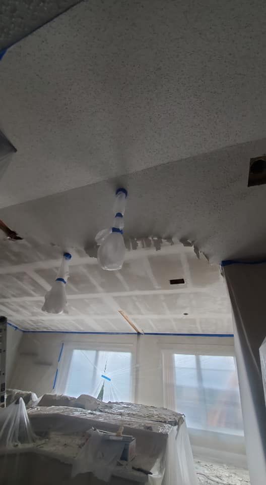 A room under renovation with taped and masked ceilings and windows, and dust-covered furniture.