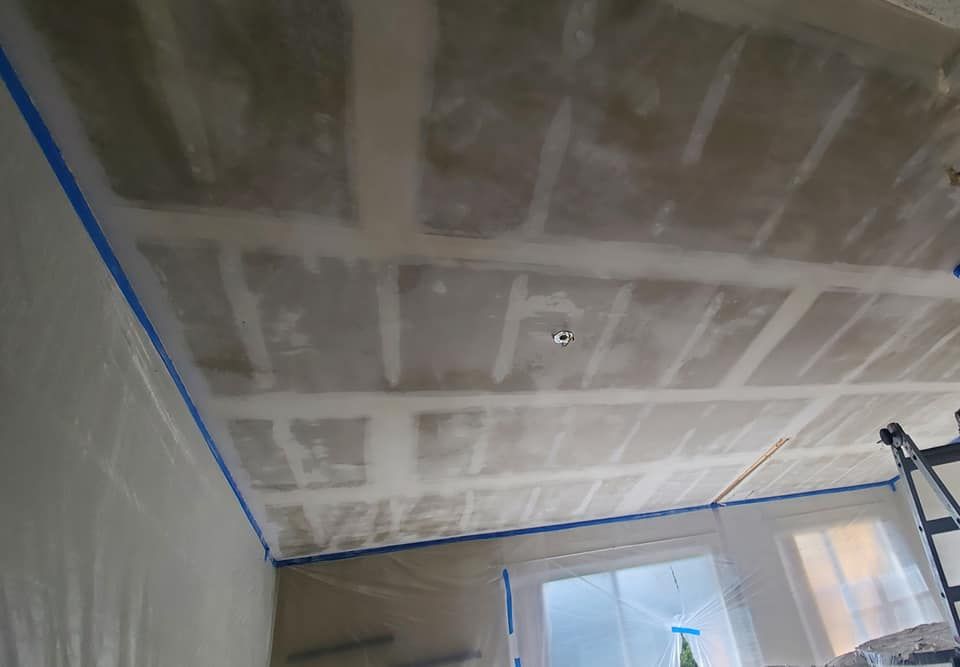 A ceiling undergoing drywall renovation with visible joint compound on the seams, prepared for painting with blue tape.