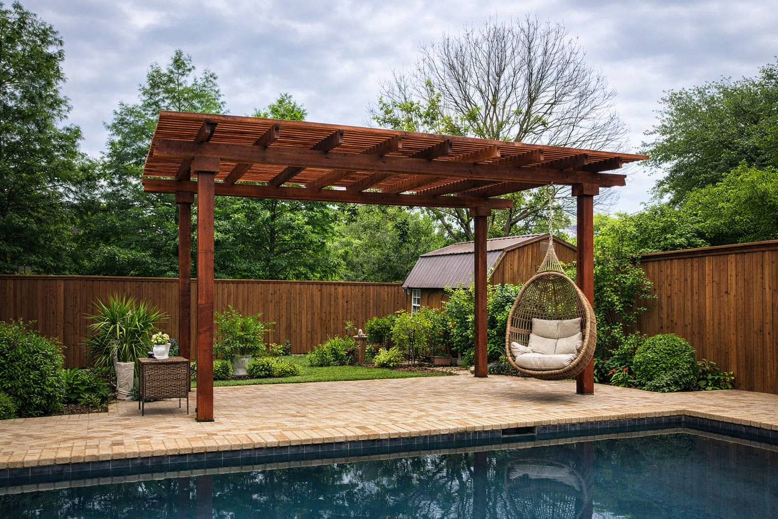 Backyard with green lawn, stone patio, brick house, and pergola under a sunny sky.