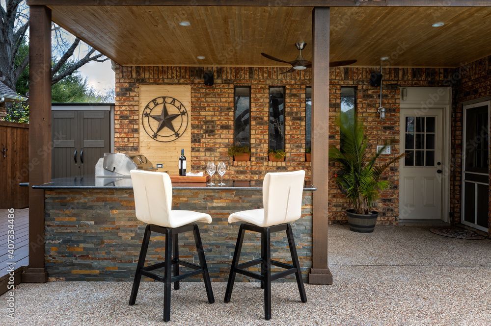 Outdoor kitchen on a deck with grill, sink, and countertop, overlooking trees.
