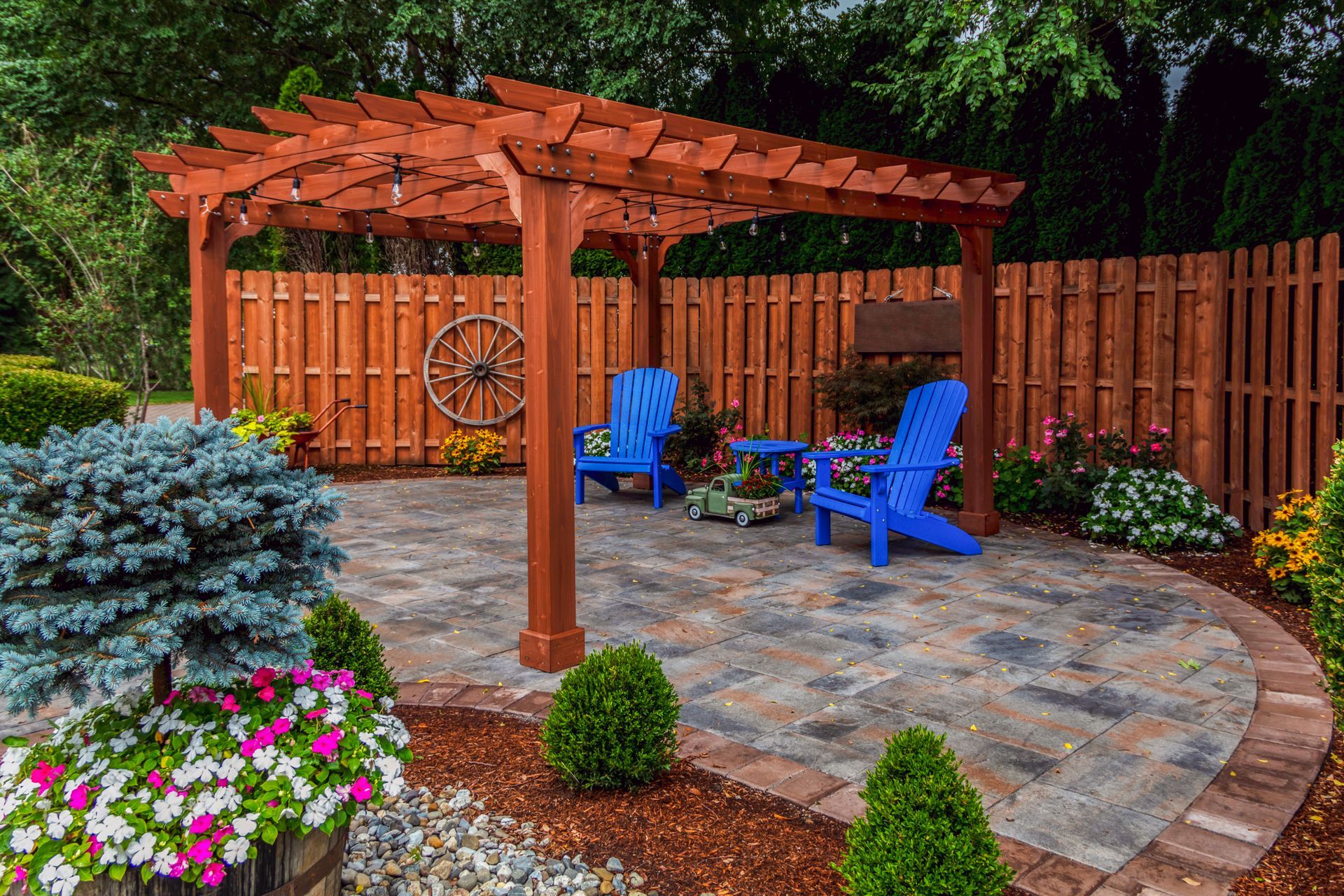 Stone patio in a garden with lawn, dining set, and hanging chair surrounded by trees and colorful foliage under a cloudy sky. Stone patio in a garden with lawn, dining set, and hanging chair surrounded by trees and colorful foliage under a cloudy sky.