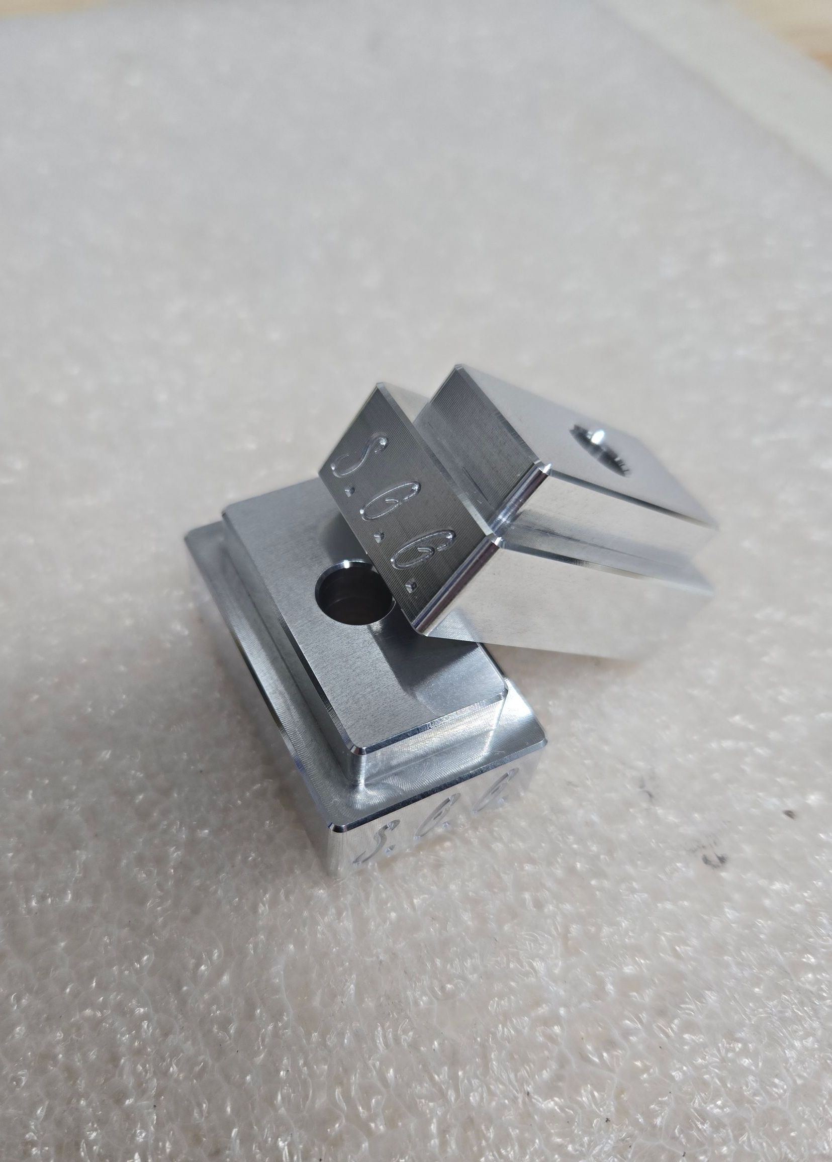 Two silver metal blocks stacked, each with a hole and stepped edges.