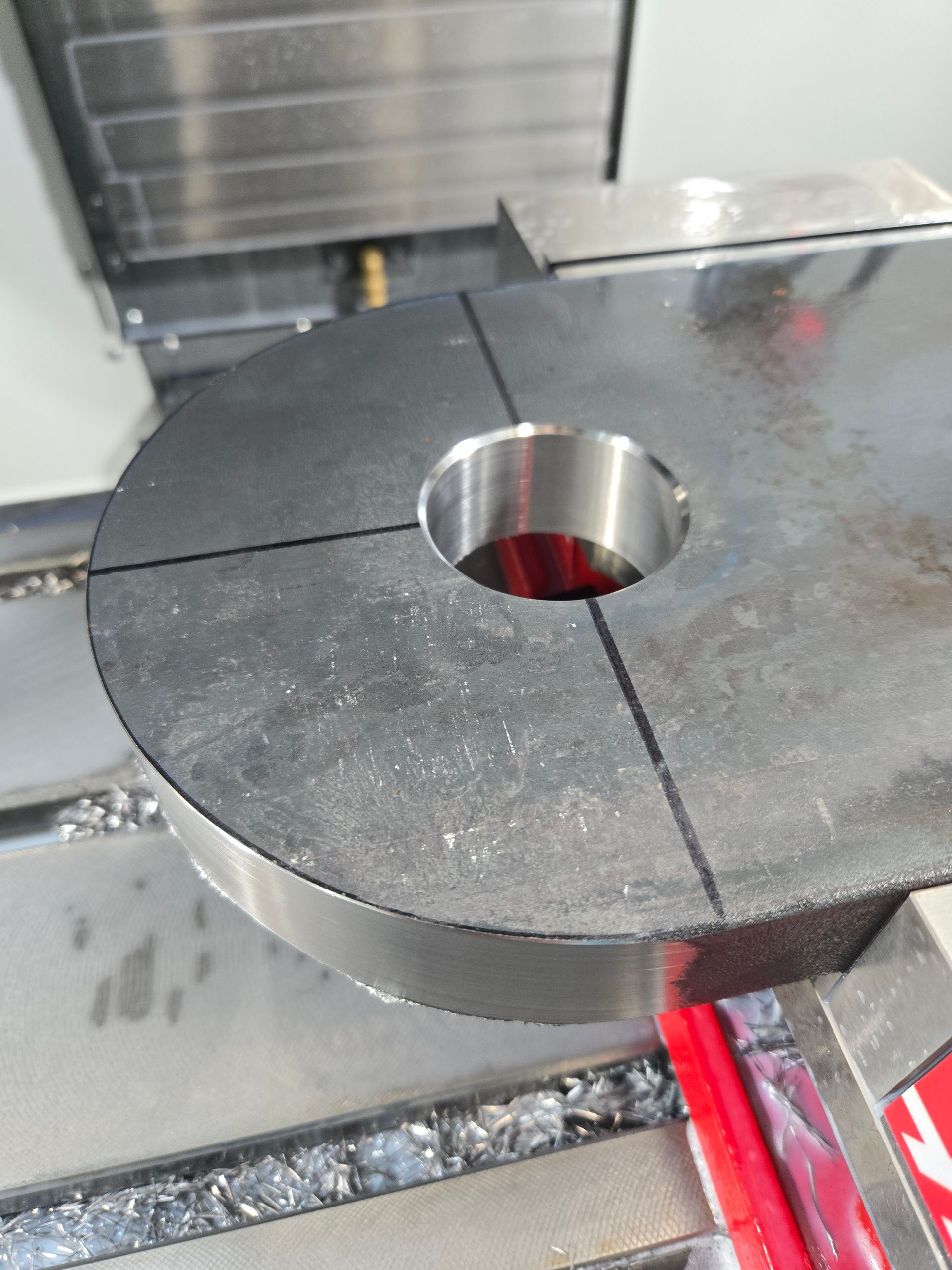 A metal workpiece in a machine vise, with a central hole and marked lines.
