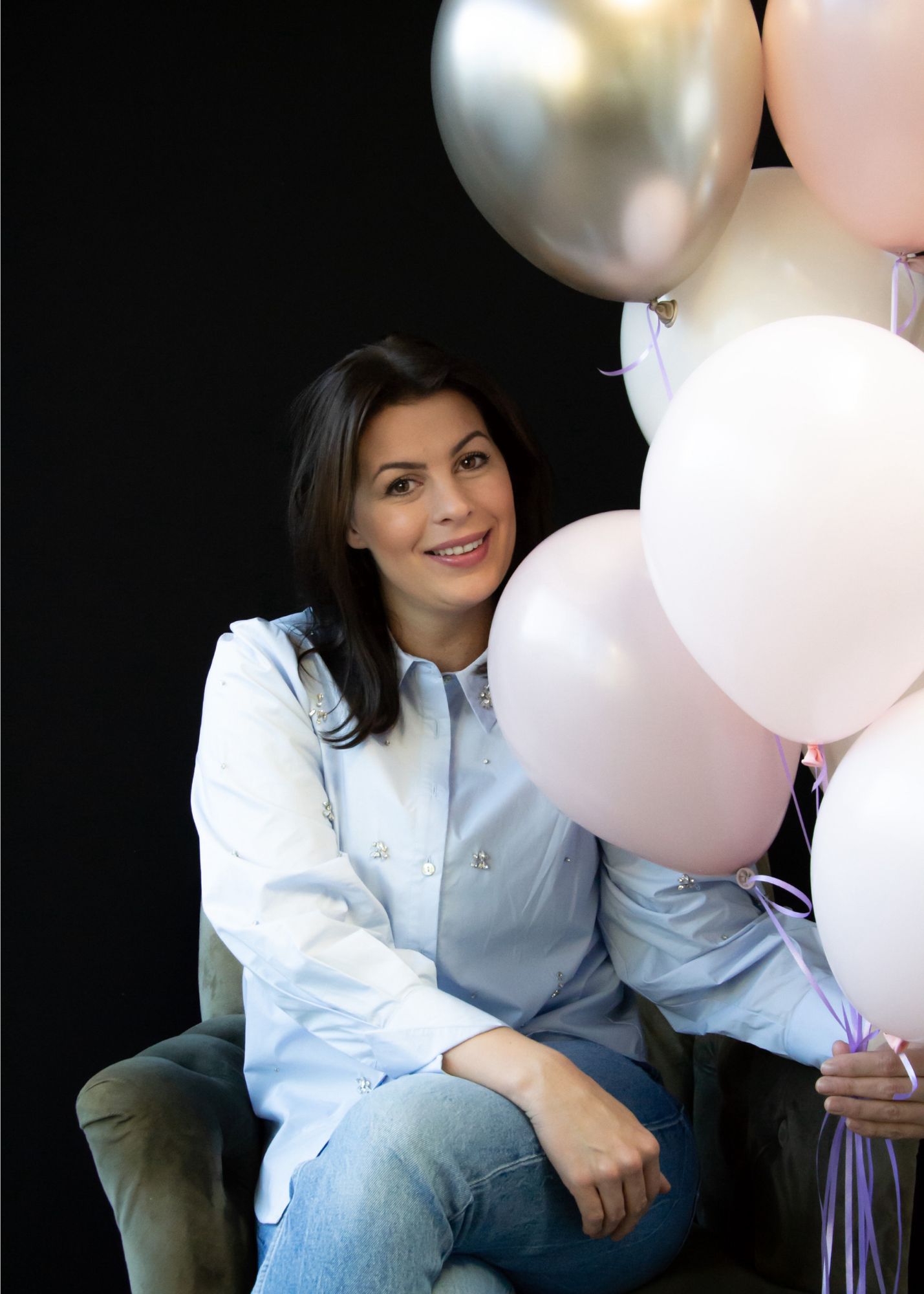 Een vrouw zit op een stoel met een bos ballonnen in haar handen.