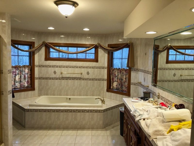 A bathroom with a tub , sink , mirror and window.
