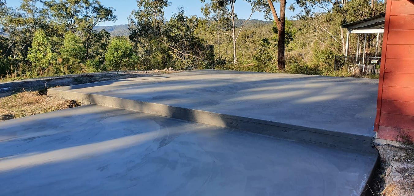 A concrete driveway with a red building and trees in the background. — MidCoast Concreting in Mount George, NSW