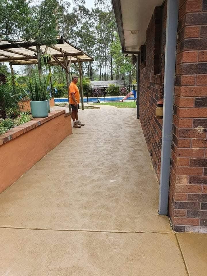 A Man is Standing on a Sidewalk Next to a Brick Building — MidCoast Concreting in Old Bar, NSW