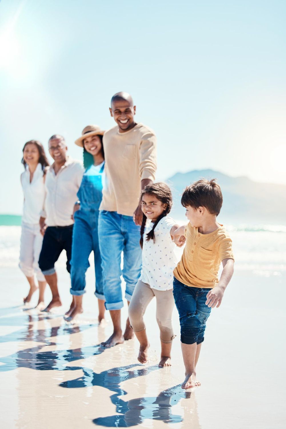 Family walking on a beach, smiling. Sunshine, ocean in background.