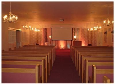 Church sanctuary with wooden pews, chandelier lights, and a projection screen at the front