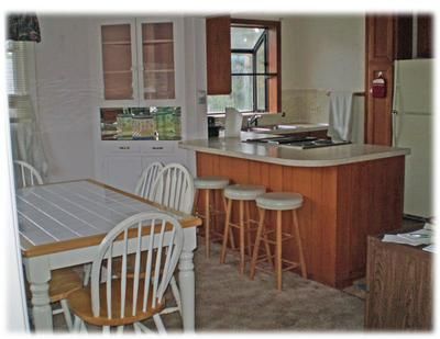 Dining area and kitchen with white chairs, wooden island stools, and beige walls