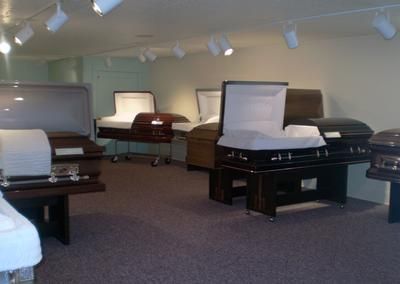 Showroom with several closed caskets displayed on stands under bright ceiling lights