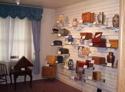 Museum display room with shelves of pottery, books, and artifacts along a white paneled wall.